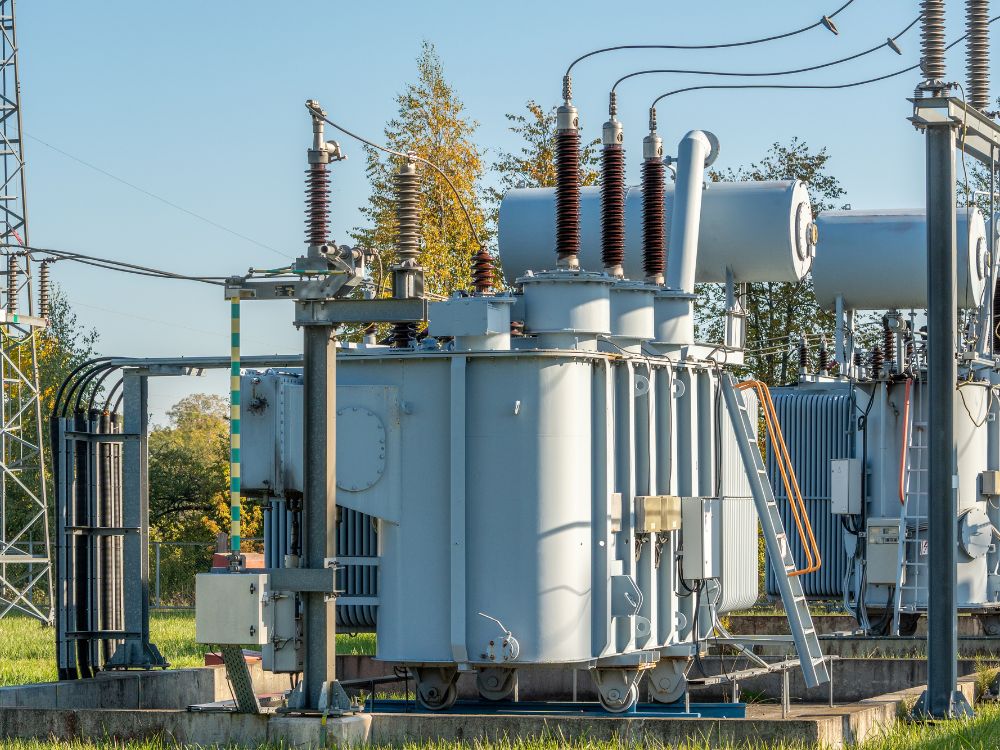 Imagem de transformadores industriais em uma subestação, exemplificando a aplicação em larga escala e a escolha entre transformador ou autotransformador.
