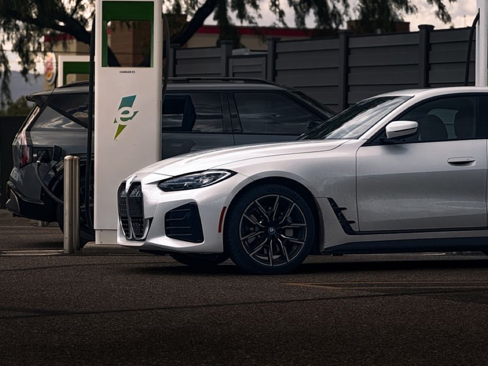 Dois carros elétricos estacionados junto a uma estação de recarga pública, ilustrando a infraestrutura necessária para carregar veículos.