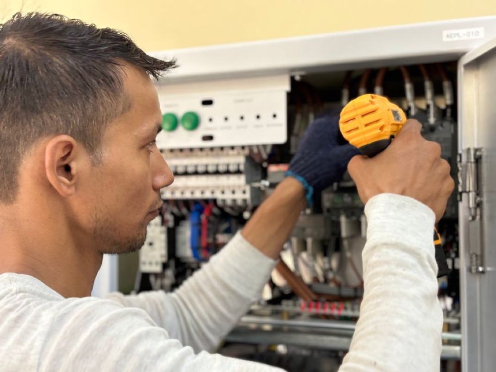 Profissional utiliza uma ferramenta de medição diante de um painel elétrico aberto durante uma inspeção de componentes e conexões. Tudo para explicar qual transformador usar para ar-condicionado de 12.000 BTUs.